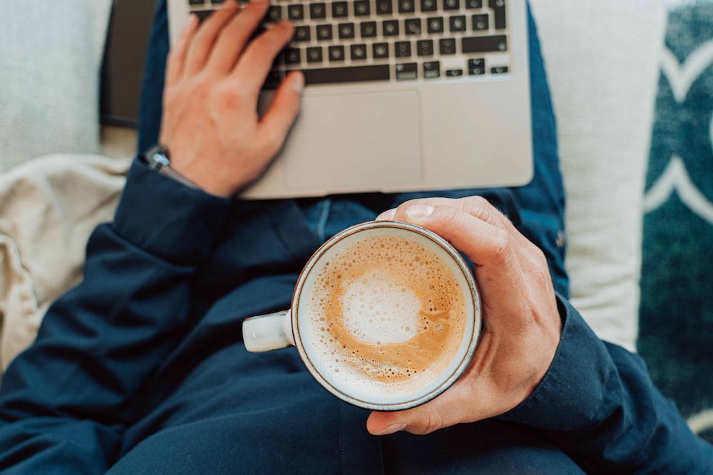 Person holding white ceramic mug with brown liquid